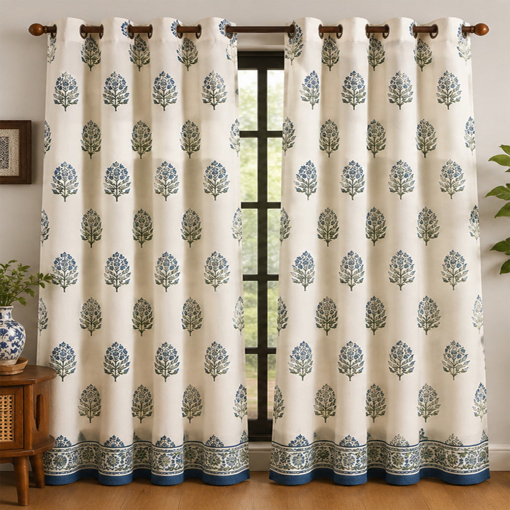 White curtain with blue floral pattern in a room with wooden floor and plant.