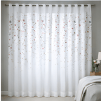 White floral curtain in a room with a bed and lamp.