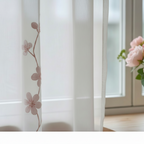 Sheer curtain with floral pattern in a room with a window and flowers.